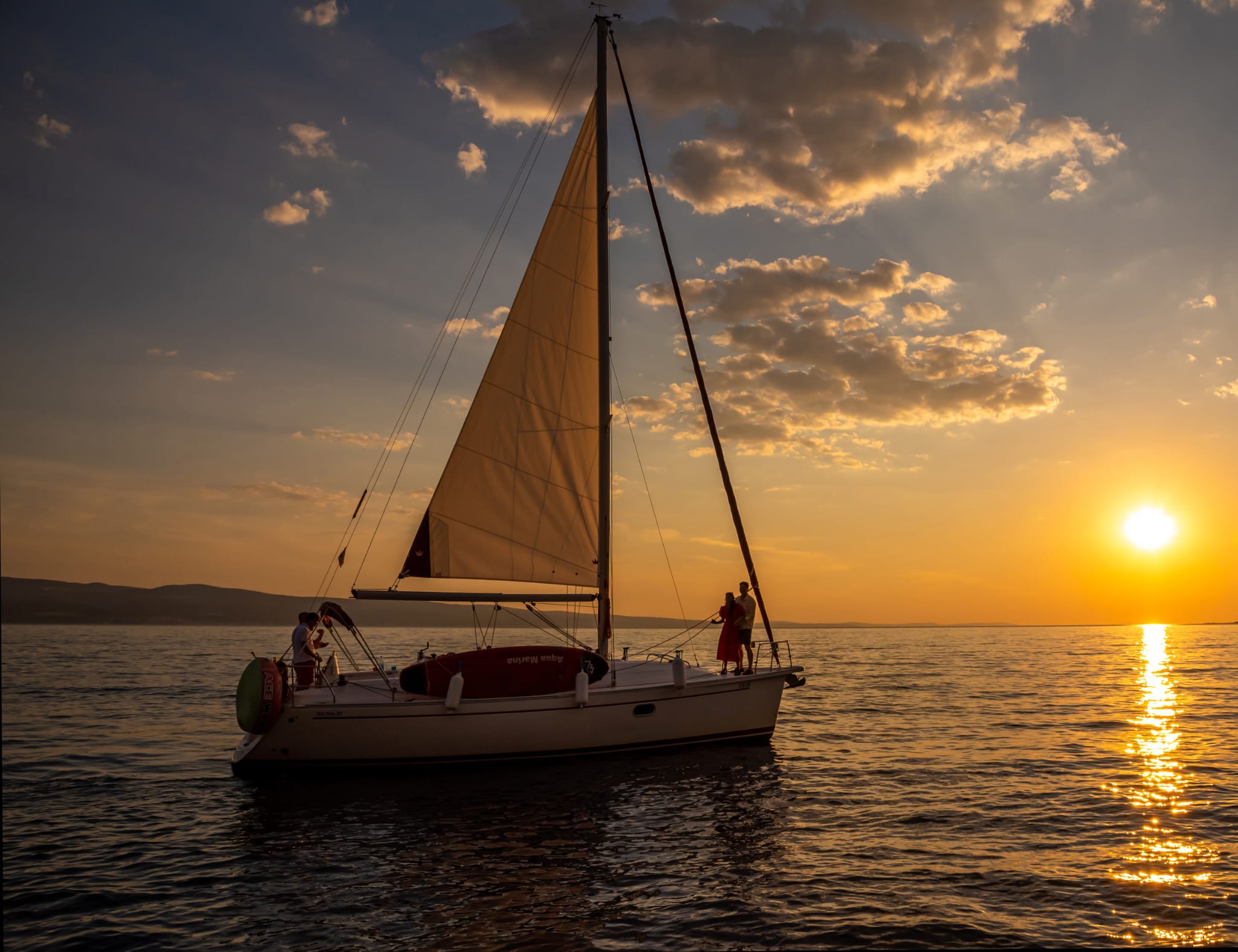 A couple silhouetted on the bow as the sun sets over the sea